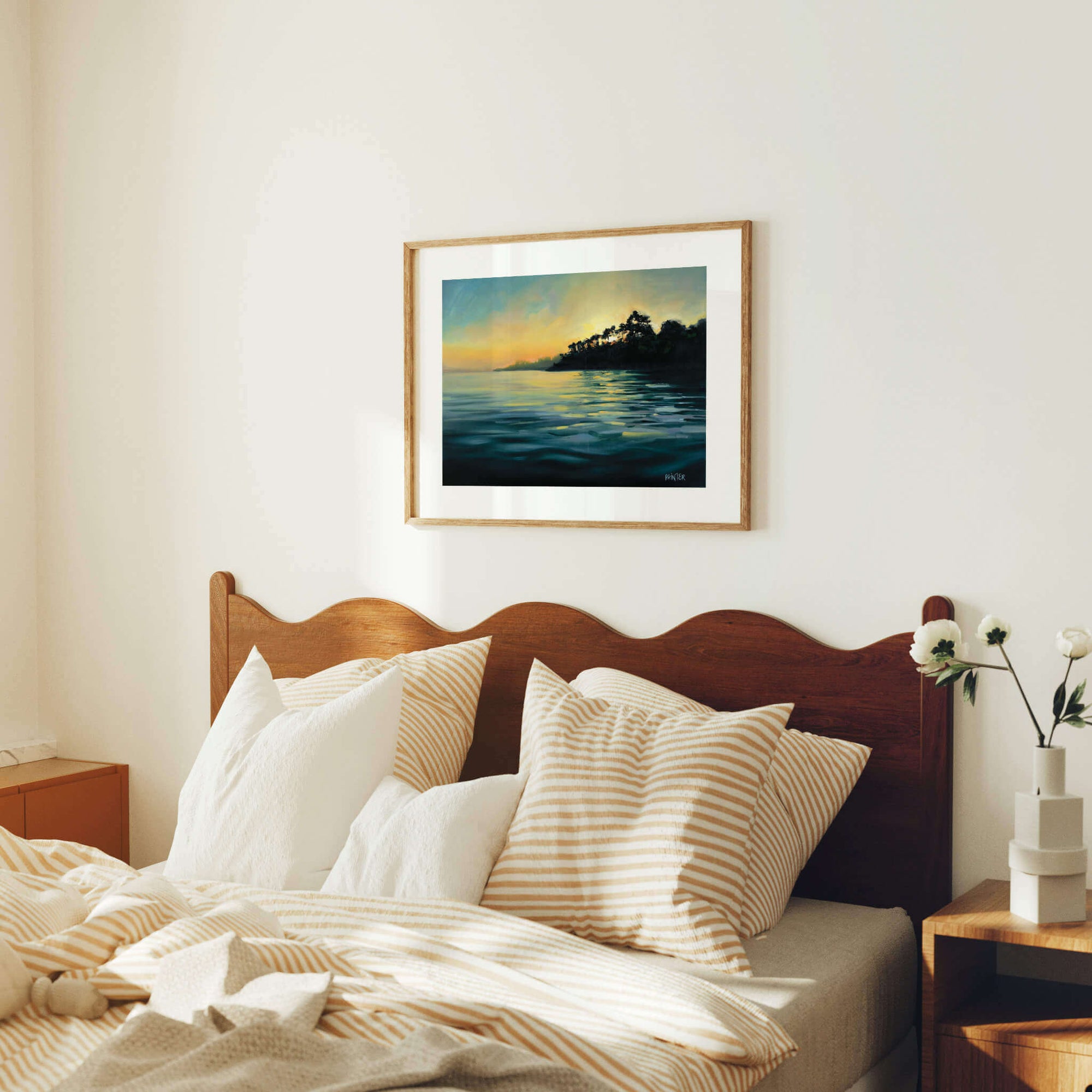 Bedroom with wooden headboard, pillows, and a framed painting of a sunset over water.