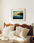 Bedroom with wooden headboard, pillows, and a framed painting of a sunset over water.
