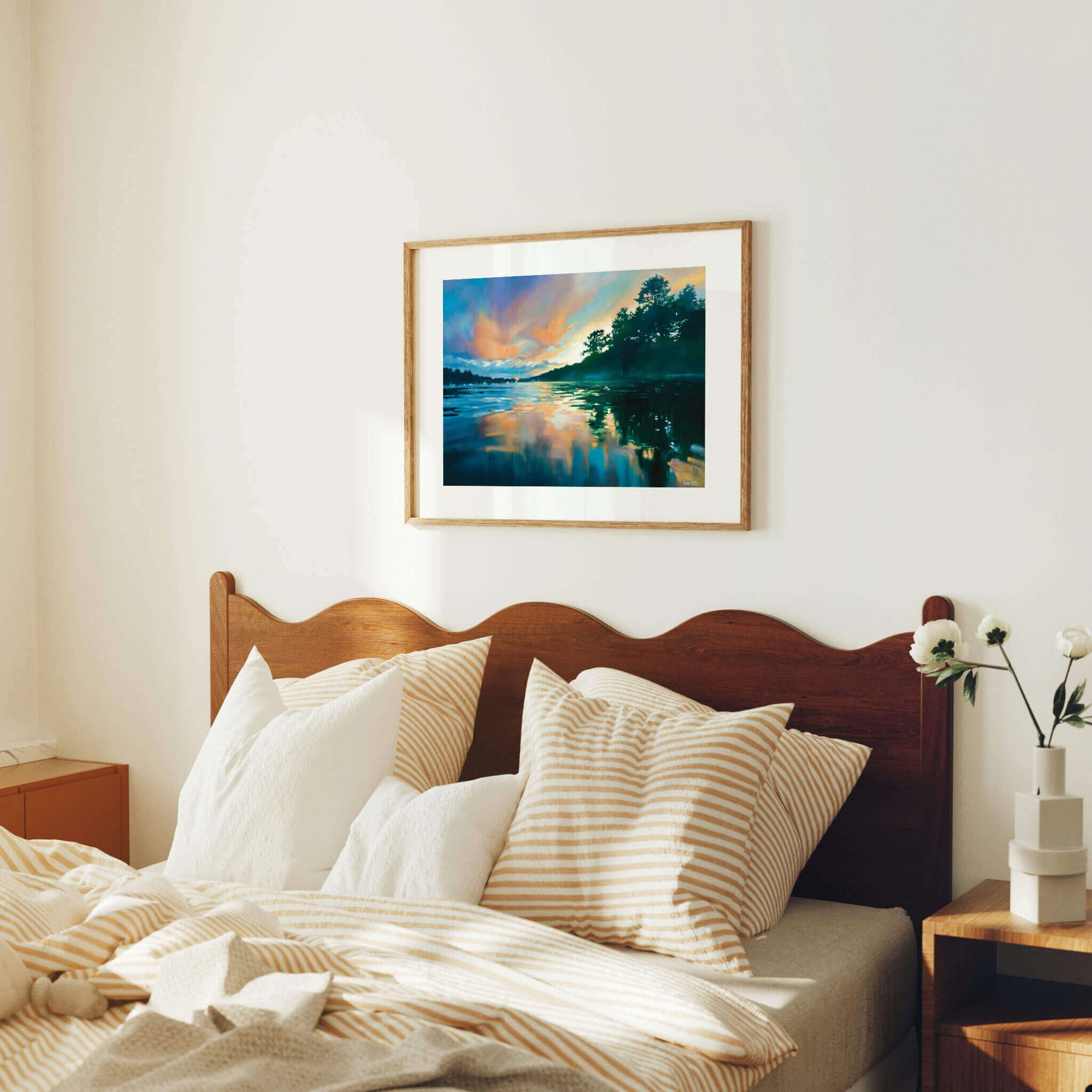 Bedroom with wooden headboard, pillows, and a framed landscape painting on the wall.