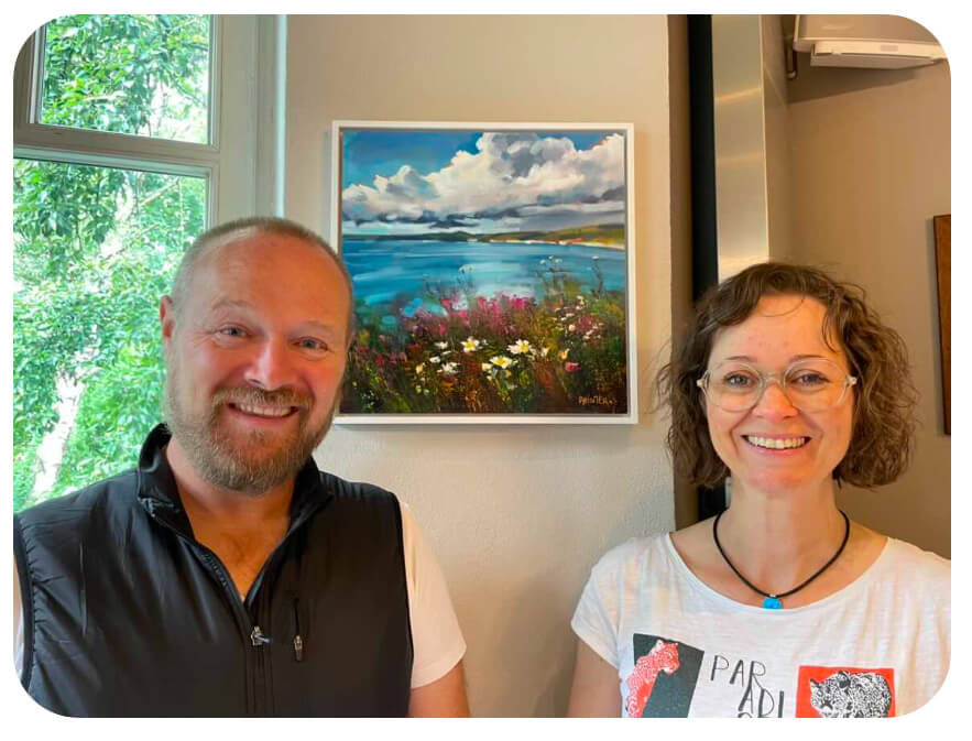 Two collectors standing in front of their new oil painting of a Cornwall landscape on their wall.