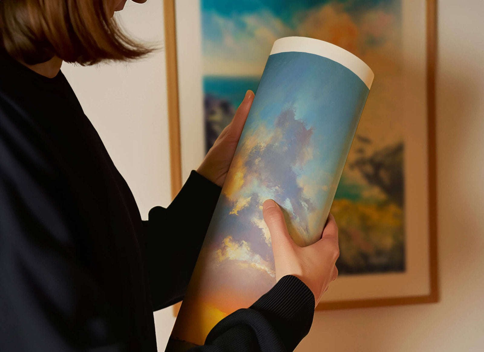 Person holding a rolled fine art paper print with a shimmering sunset scene in front of a framed art print.