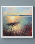 Framed warm painting of a sunset over water with a tree on a cool blue neutral wall