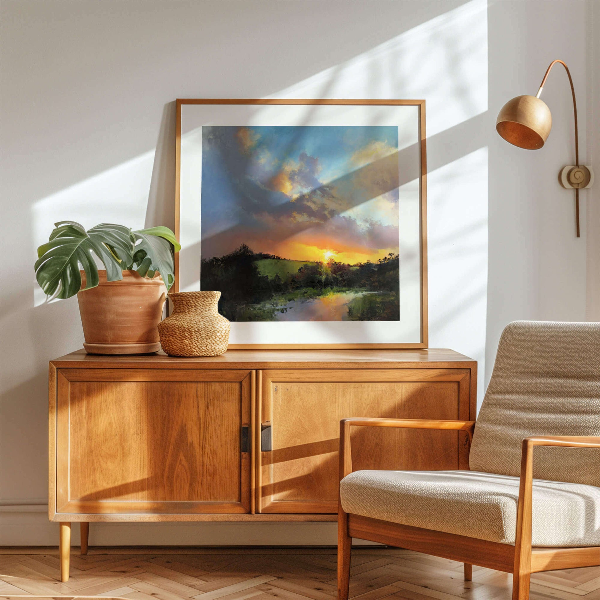 Wooden sideboard with a landscape art print, plant, and chair in a bright room - by Rachel Painter, contemporary artist