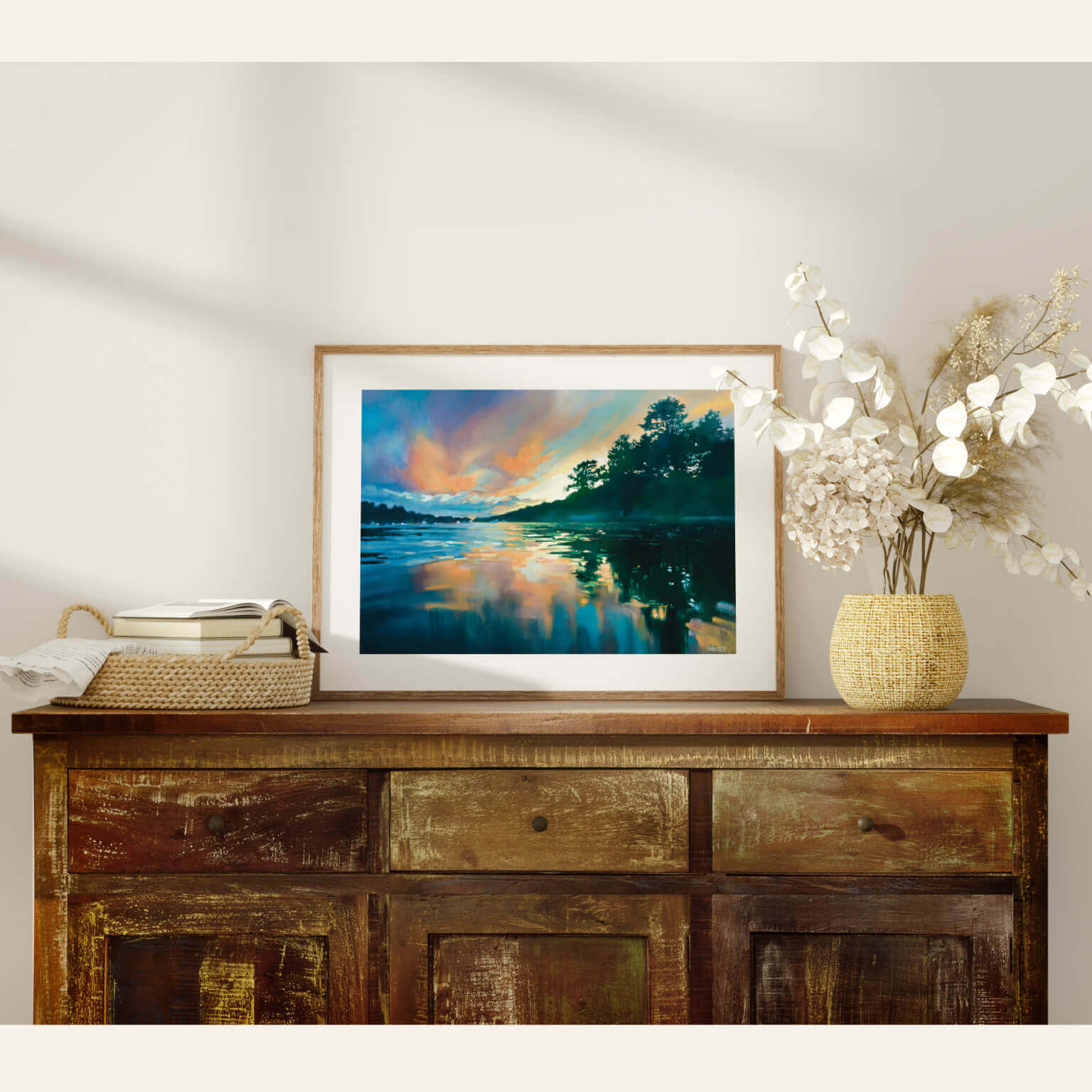 Framed artwork of a landscape print on a wooden sideboard with decorative items.