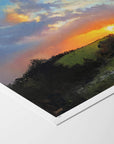 Fine art paper print with white border of a landscape with a colourful sky and green hillside.