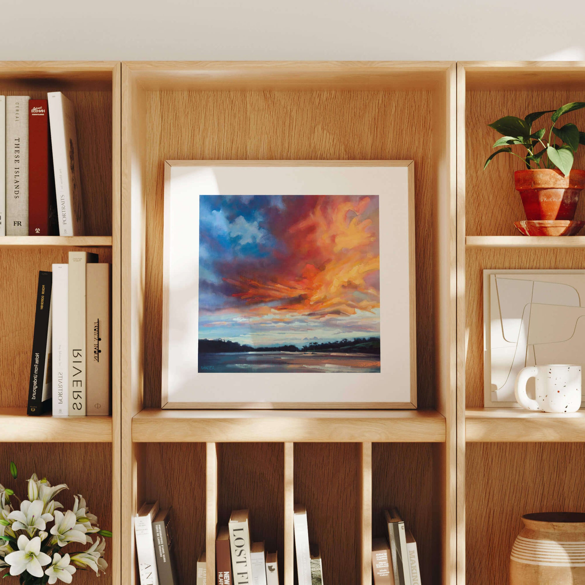Framed artwork on a wooden bookshelf with books and decorative items.