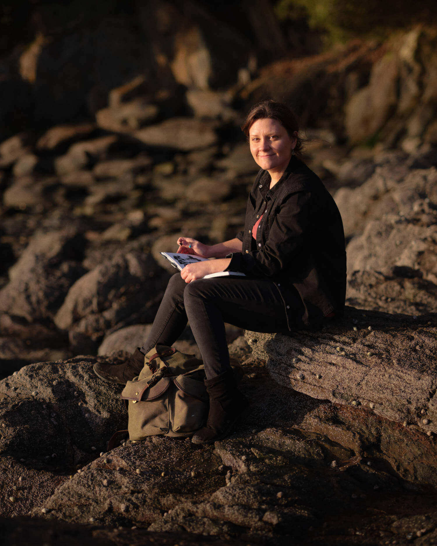 Rachel sitting on rocks sketching outdoors in charcoal as inspiration for original art for sale