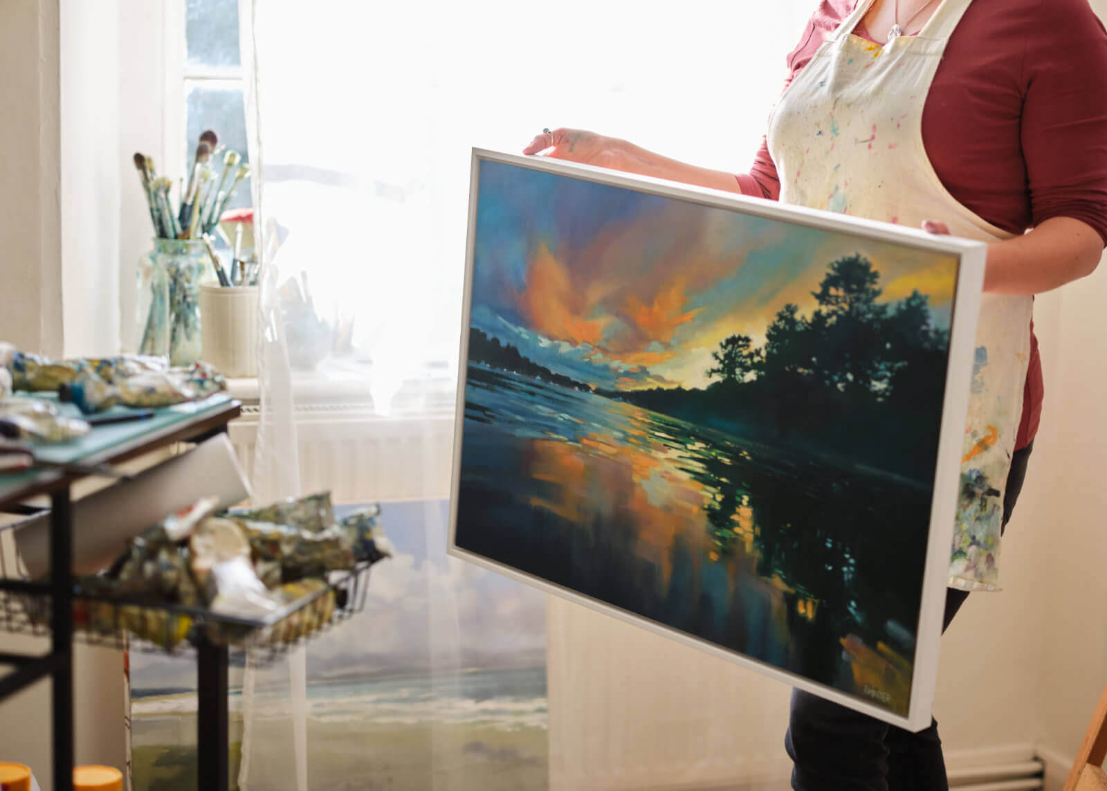 Rachel holding an original landscape painting of Cornwall of the Helford River